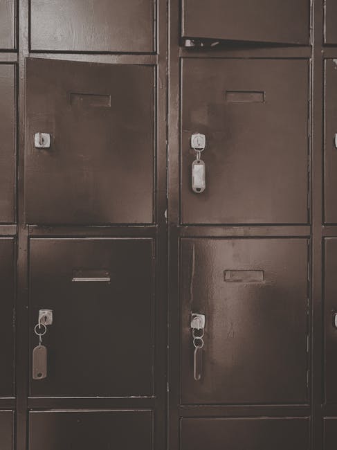 A close-up view of a set of dark brown metal lockers with small rectangular nameplates and keyholes on each door. Some lockers have padlocks or keys inserted, indicating they are secured. The lockers are arranged in a grid pattern, likely located in a storage area or hallway used for secure house removals or relocation services. The image does not show any other objects or actions, focusing solely on the locker fronts, which are evenly lit and have a matte finish. This setting may reflect storage solutions involved in packing and storing belongings during a house move managed by Man with Van Kew, supporting secure short-term storage options near Kew.